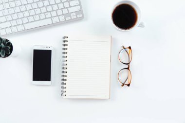 Laptop bilgisayarlı modern beyaz ofis masası, siyah ekranlı akıllı telefon bir defter ve bir fincan kahve. Kopyalama alanı olan üst görünüm, düz uzanma.