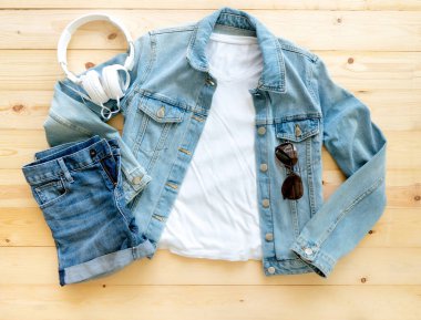 Kahverengi ahşap arka planda beyaz tişört, kot pantolon ve kulaklık. Şablon, düz yat