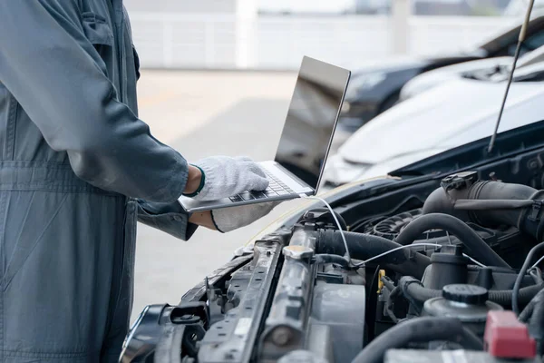 Skilled mechanic using a laptop computer to check collect information during work a car engine. service maintenance of industrial to engine repair.