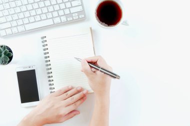 Modern beyaz ofis masasında klavye bilgisayarı, defter, ağaç, bardak ve kahve ile çalışan bir iş adamı. Kopyalama alanı olan üst görünüm, düz yatay. 