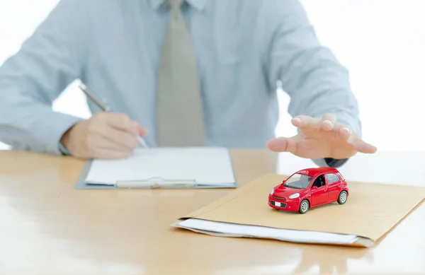Car on document envelope with man signing purchase documents in background. while hand complete the insurance policy, rental documents and loan document. concept guy buying new car