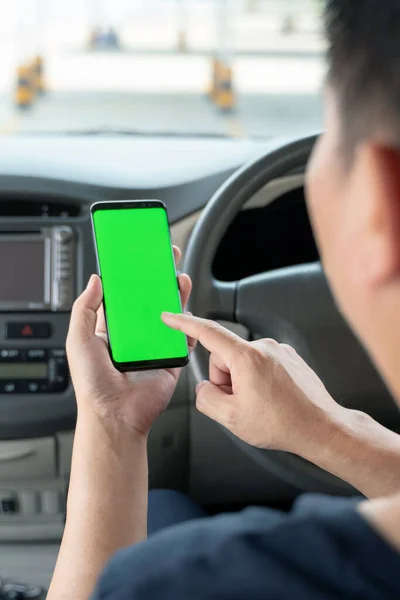 Mock up of man using mobile smart phone inside a car. Driver hand holding blank green screen smartphone, searching address and pin location via map navigator application, transportation technology