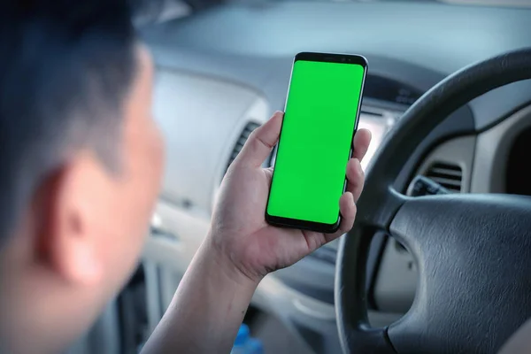 Mock up of man using mobile smart phone inside a car. Driver hand holding blank green screen smartphone, searching address and pin location via map navigator application, transportation technology
