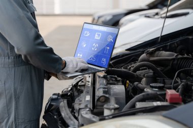 İş sırasında bilgi toplamak için dizüstü bilgisayar kullanan yetenekli bir tamirci. Bir araba motoru. Endüstriden motor tamirine servis bakımı. 