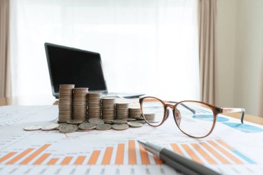 Bilgisayarlı ve bozuk para yığınlı iş belgeleri ve grafik finansal diyagramı.