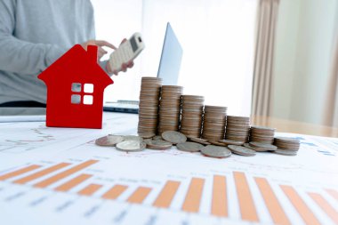 İş adamı verileri analiz etmek için hesap makinesi kullanıyor. Masanın yanındaki dizüstü bilgisayarda bozuk para, ev tasarımları, grafikler ve gözlükler var. Yatırım fikirleri.