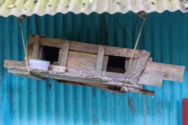 Kırsal eski ahşap kuş yuvası ya da evcil güvercinler için barınak. Bangladeş 'teki bir köy evinin teneke çatısının altındaki mavi kıvrımlı metal bir duvara karşı iple asılı. Kültürel mimari.