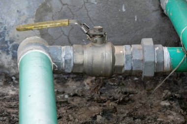 Bangladeş 'teki yerleşim su tedarik ve dağıtım sisteminin bir parçası olarak kurulmuş yeşil bir PVC plastik borudaki akışı kontrol eden elle kontrol edilen top valfinin yakın görüntüsü.