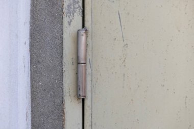 Yakın planda paslanmaz çelik kapı donanımı var. Görünür çiziklerle kaplı gri beton bir duvara tutturulmuş bir menteşe var. Mimari ve inşaat geçmişi ayrıntıları.