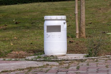 Bir tatil beldesinin kaldırım kenarına yerleştirilmiş, yeniden tasarlanmış, beyaz plastik bir varil veya varil. Geri dönüşüm, atık yönetimi ve çevre kavramı.