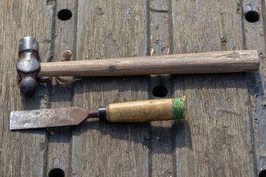 Eski, geleneksel el aletlerinin yakın çekimi: sağlam bir vintage çekiç ve eski bir metal keski, patina ve yaşı gösteriyor. Ahşap işçiliği, marangozluk ve genel inşaat işleri için gerekli ekipmanlar.