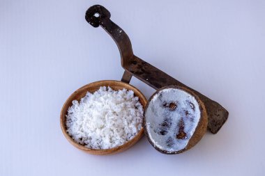 Tahta bir kasede taze rendelenmiş organik hindistan cevizi eti ile geleneksel hindistan cevizi kazıyıcısı. Beyaz arka planda kazınmış kabuk ve parçalanmış hindistan cevizi. Otantik Güney Asya mutfak aleti ve yiyeceği