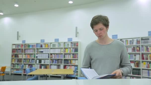 Jonge man die boek leest in de bibliotheek — Stockvideo