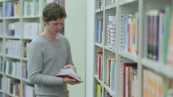 Estudiante tomando libro de estantería en la biblioteca — Vídeos de Stock