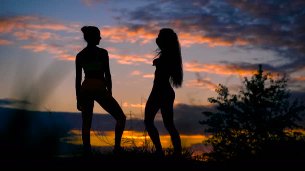 Дві стрункі дівчата відпочивають після бігу і спостерігають за заходом сонця — стокове відео