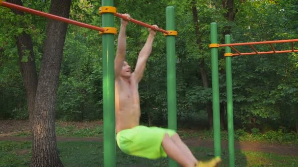 Estilo de vida desportivo, treino de rua. Homem musculoso a fazer um exercício para o tronco no bar. Campo de esportes ao ar livre . — Vídeo de Stock