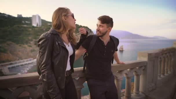 De jongen en het meisje in een leren jas, staande op het balkon met uitzicht op de zee en de kliffen. — Stockvideo