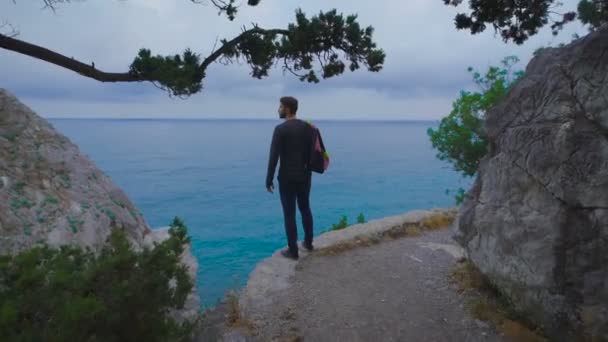 Jeune hipster avec sac à dos adapté au bord et regarde les vues imprenables . — Video