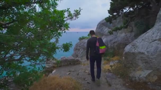 Jovem hipster com mochila adequada à borda e olha para as vistas deslumbrantes . — Vídeo de Stock