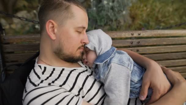 Vater und kleiner Sohn ruhen sich im Park auf einer Bank aus. — Stockvideo