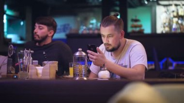 Şirin yenilikçi bir gece kulübünde bir masada oturur ve bir şey üstünde smartphone basar.