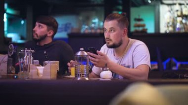 Şirin yenilikçi bir gece kulübünde bir masada oturur ve bir şey üstünde smartphone basar.