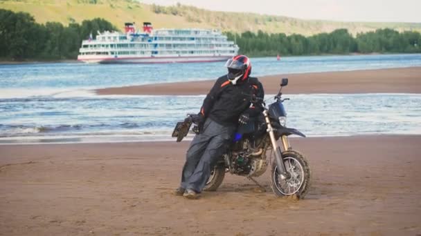 Motociclista descansando na margem do rio ao lado de sua motocicleta . — Vídeo de Stock