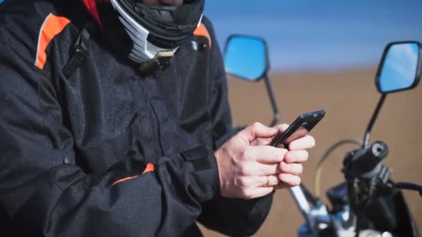 バイカーは彼のバイクの横にある、川の銀行で、彼は携帯電話を探しています. — ストック動画