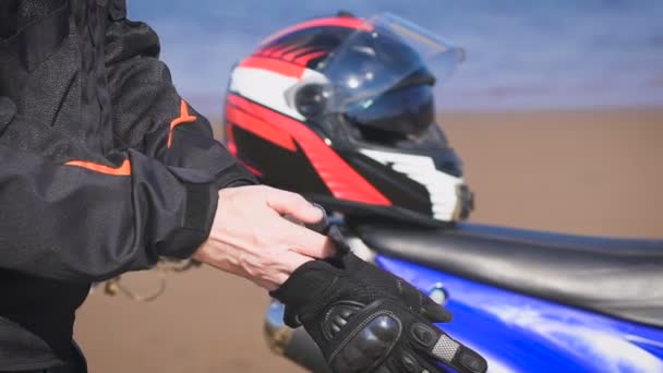 Motociclista en la calle junto a su bicicleta, se pone guantes . — Vídeos de Stock