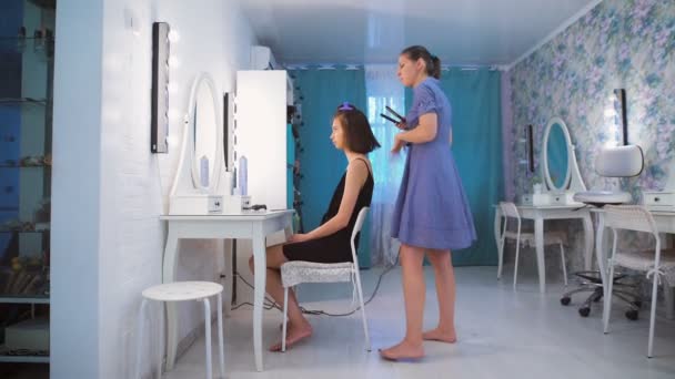 Cabeleireiro pentear o cabelo de uma bela jovem morena . — Vídeo de Stock