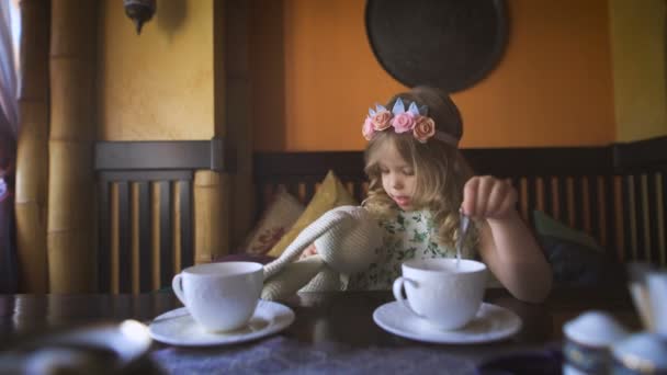 Una niña está tomando el té con su conejo de peluche en un acogedor café . — Vídeo de stock