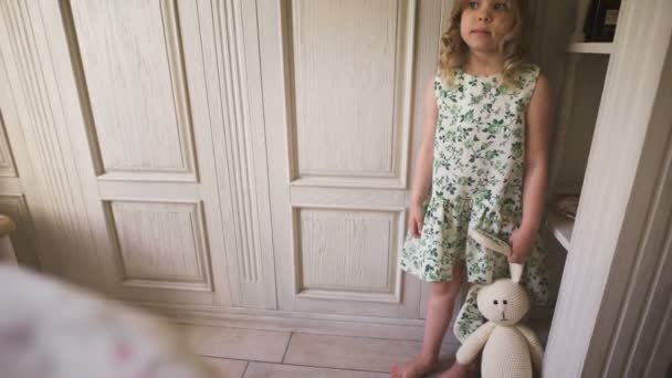 Uma menina bonita em pé em uma sala branca segurando um coelho de pelúcia — Vídeo de Stock