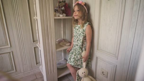 Uma menina no vestido parece pensativo de pé o quarto brilhante — Vídeo de Stock