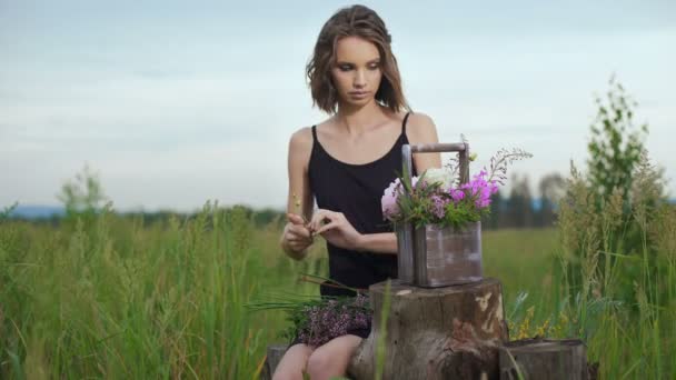 Стройная девушка в черном платье работает цветы на закате — стоковое видео