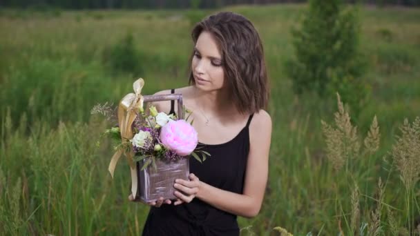 Verse bloemen in een stijlvolle lade. Mooie brunette in een bloemrijke veld in de avond. — Stockvideo