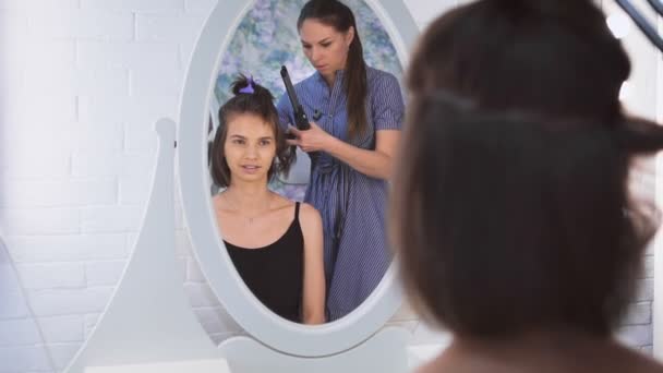 A beautiful woman looking at a mirrow while a stylist is making her hair. — Stock Video