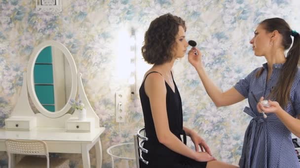 Joven artista de maquillaje femenino que trabaja en el estudio brillante, aplicando maquillaje a un cliente — Vídeos de Stock