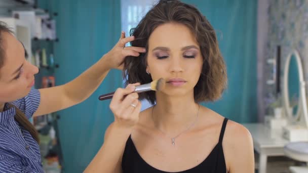 Joven artista de maquillaje femenino que trabaja en el estudio brillante, aplicando maquillaje a un cliente — Vídeos de Stock