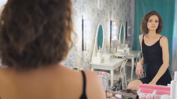 Eine schöne junge Frau, die in einen Spiegel blickt und sich amüsiert. — Stockvideo