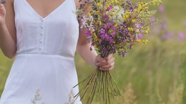 Una mujer joven de pie en el campo verde con ramo de flores — Vídeos de Stock