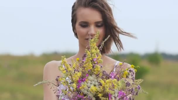 Una mujer joven de pie en el campo verde con ramo de flores — Vídeo de stock