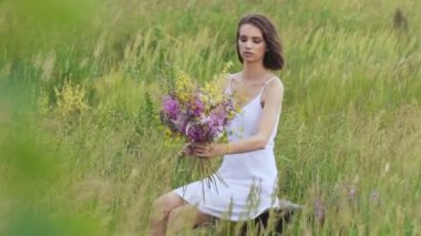 Çiçek demeti ile yeşil alanda oturan bir genç kadın