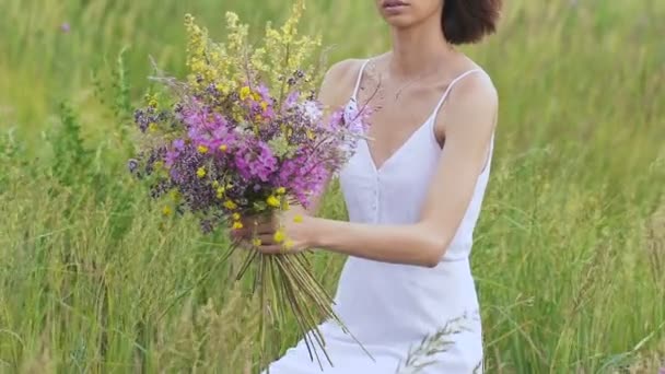 Uma jovem mulher sentada no campo verde com ramo de flores — Vídeo de Stock