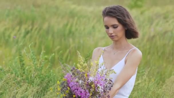 One young woman sitting on green field with flower bunch — Stock Video