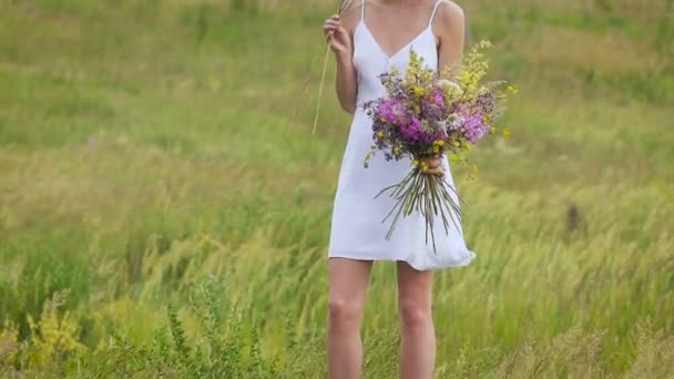 Una mujer joven de pie en el campo verde con ramo de flores — Vídeos de Stock