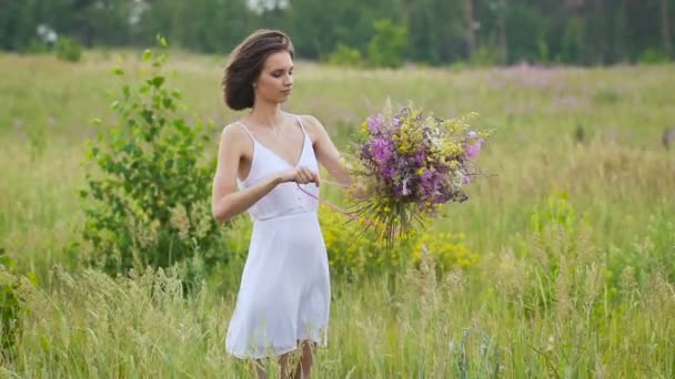 Uma jovem mulher fazendo um ramo de flores em pé no campo verde — Vídeo de Stock