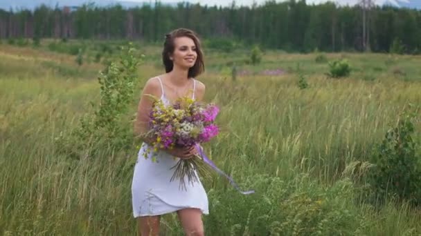 꽃다발을 즐기고 있는 녹색 들판을 걷고 있는 한 젊은 여성 — 비디오