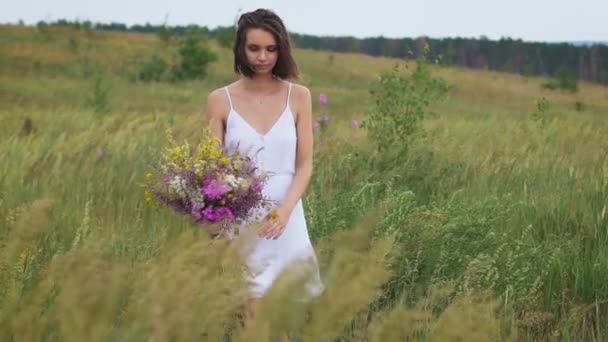 Una joven caminando en el campo verde disfrutando de un ramo de flores — Vídeo de stock