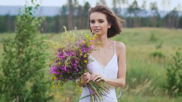 Jedna młoda kobieta stoi na zielonym polu z kwiatów pęczek — Wideo stockowe