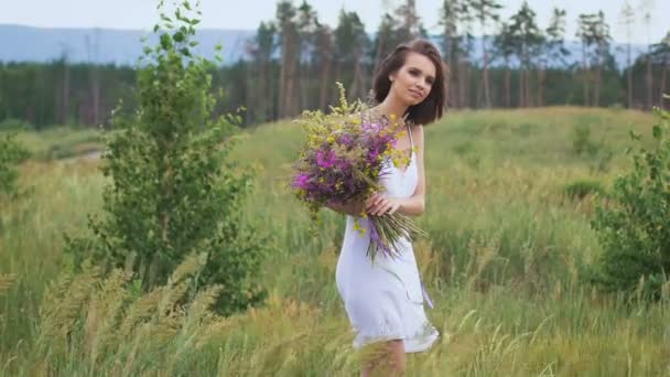 Una giovane donna in piedi sul campo verde con mazzo di fiori — Video Stock